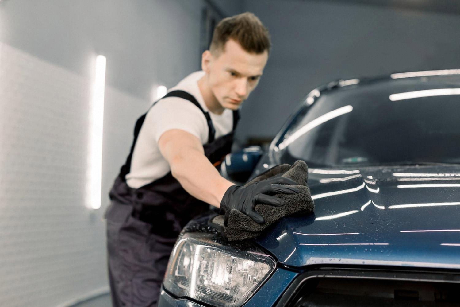 Detailer wiping a dark blue car bonnet inside a UAE workshop before window tint application