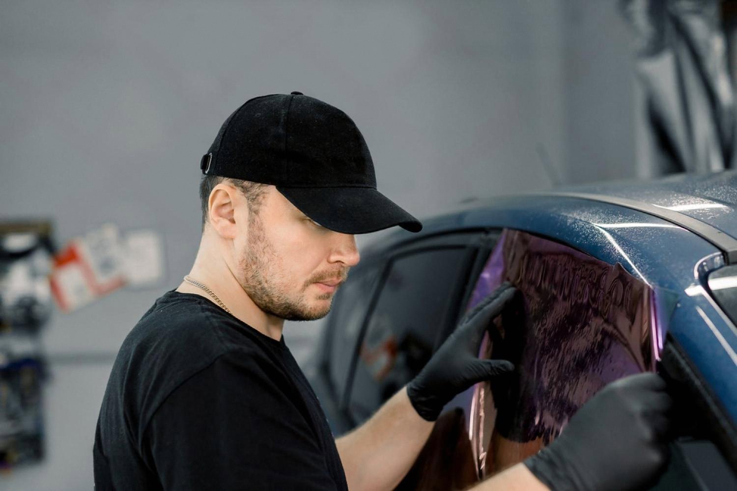 Technician in a black cap carefully applying a purple-tinted window film to a car in a UAE tinting studio